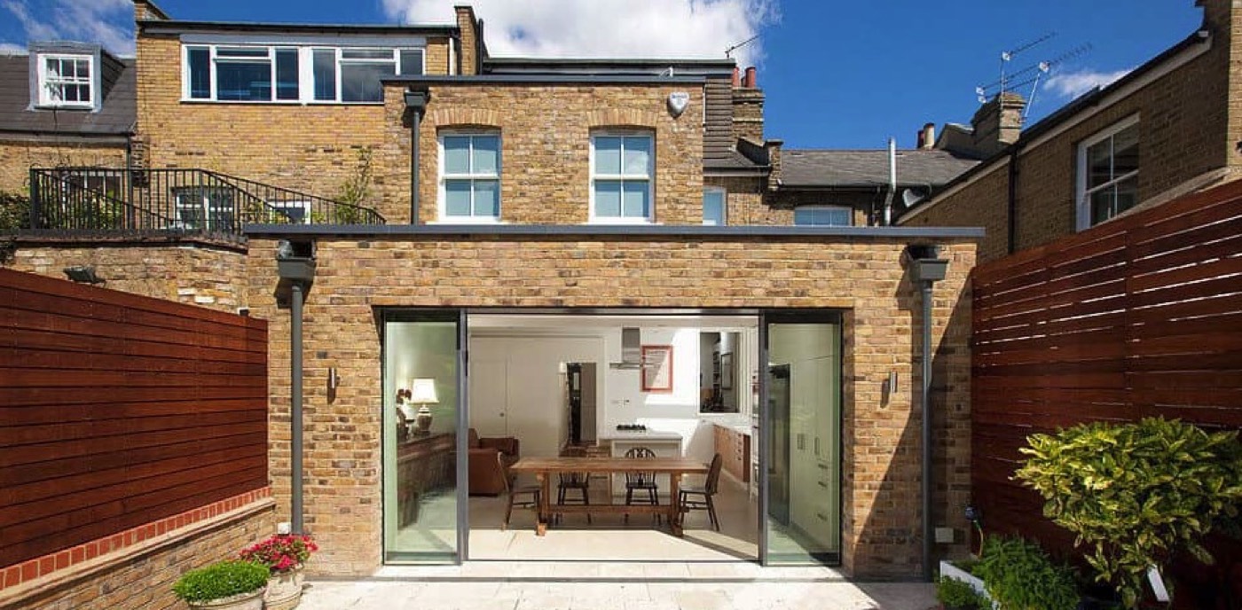 Brick-built two-storey rear extension with full-width sliding glass doors opening on to a patio
